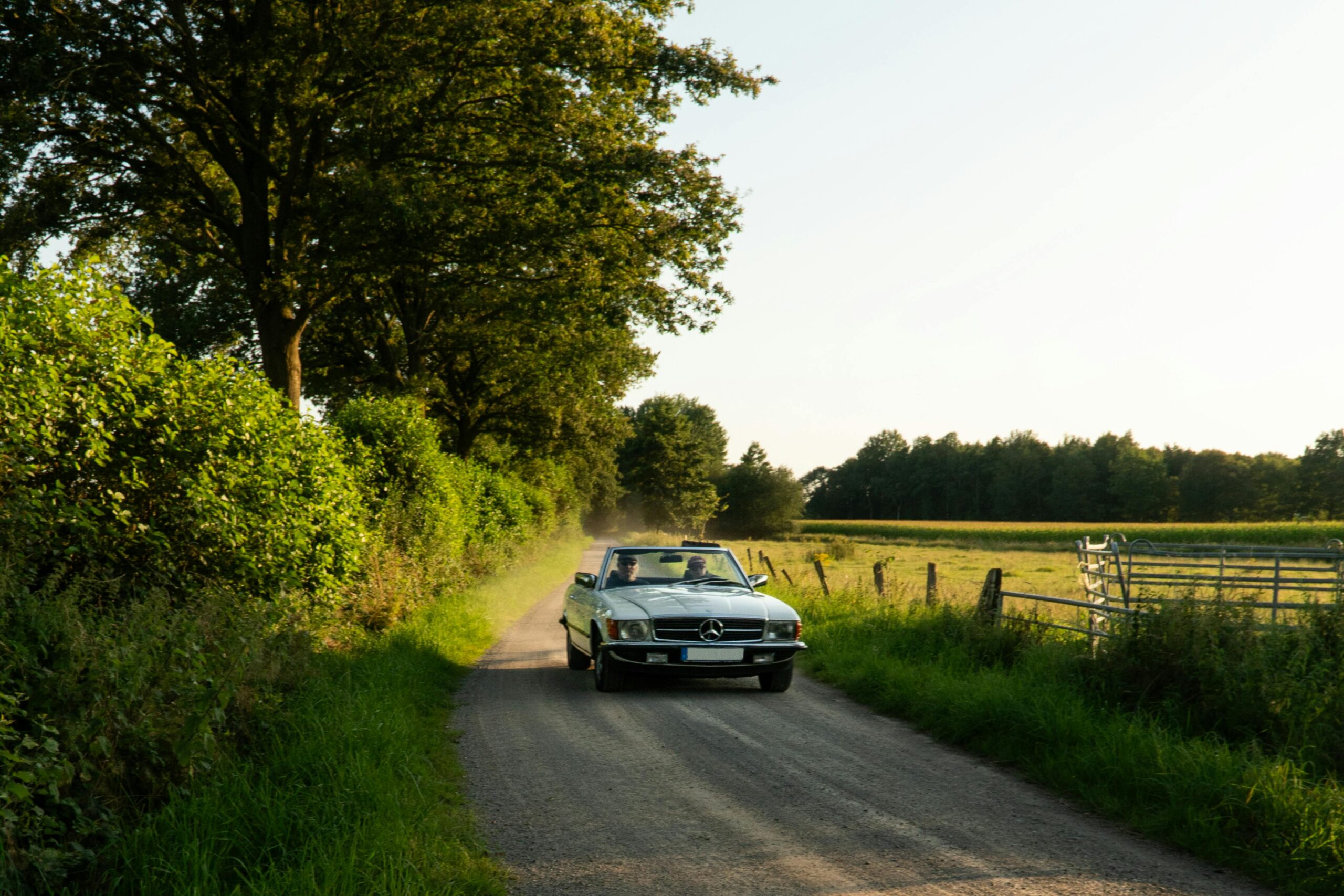 An elegant vintage Mercedes convertible driving down a scenic rural road in the summer afternoon.